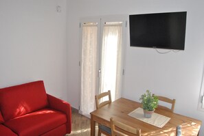 A room with a red sofa, wooden dining table, chairs, a potted plant, and a TV mounted on the wall.