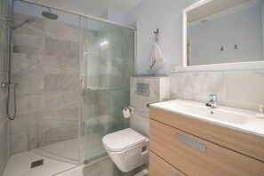 A modern bathroom with a glass shower enclosure, a white toilet, and a wooden vanity with a sink. - Apartamento Animalia (Cádiz)