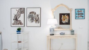 Una habitación con pared blanca, una consola de madera con una lámpara, una estantería metálica blanca y cuadros de animales enmarcados.