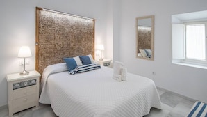Un dormitorio con una cama grande, dos mesitas de noche, un tocador, un espejo y una ventana.
