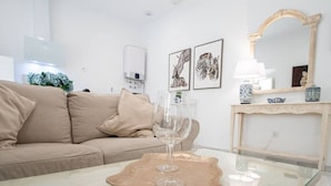 Una sala de estar moderna con un sofá color beige, una mesa de centro de vidrio con una copa de vino, una obra de arte con estampados de cebra, un purificador de aire blanco y un espejo decorativo.