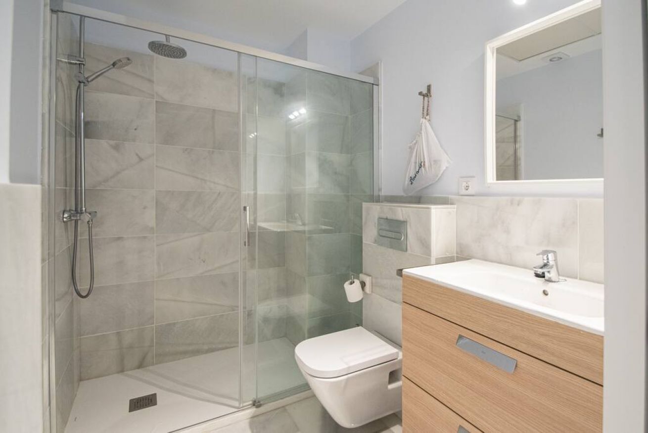 Une salle de bain moderne avec une douche à parois de verre, des toilettes blanches et un meuble-lavabo en bois doté d’un miroir.