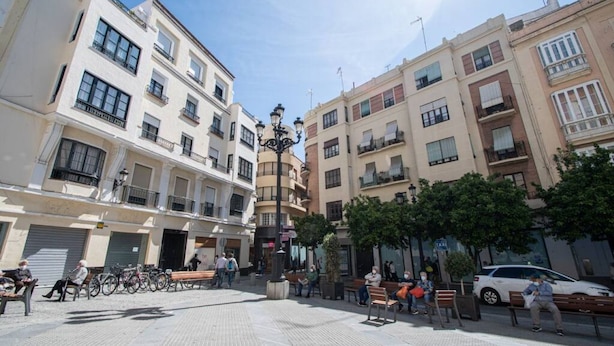 Una plaza pública con edificios, bancos y algunas personas.
