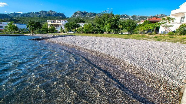 A pebbled beach with clear water, surrounded by buildings and mountains in the background. - Apartment with garden near the beach (Seline)