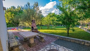 An outdoor patio with a stone table and benches, surrounded by a stone wall and greenery. - Apartment with garden near the beach (Seline)