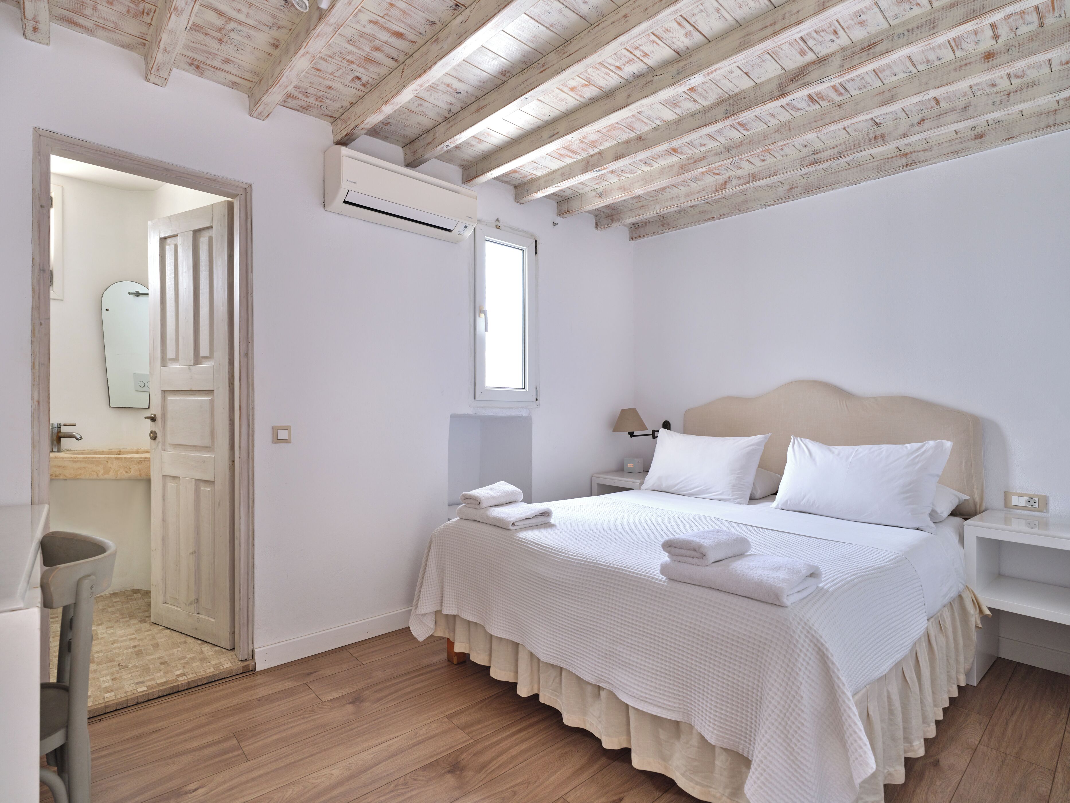A bedroom with a bed, bedside tables, a nightstand, a window, and an air conditioning unit.
