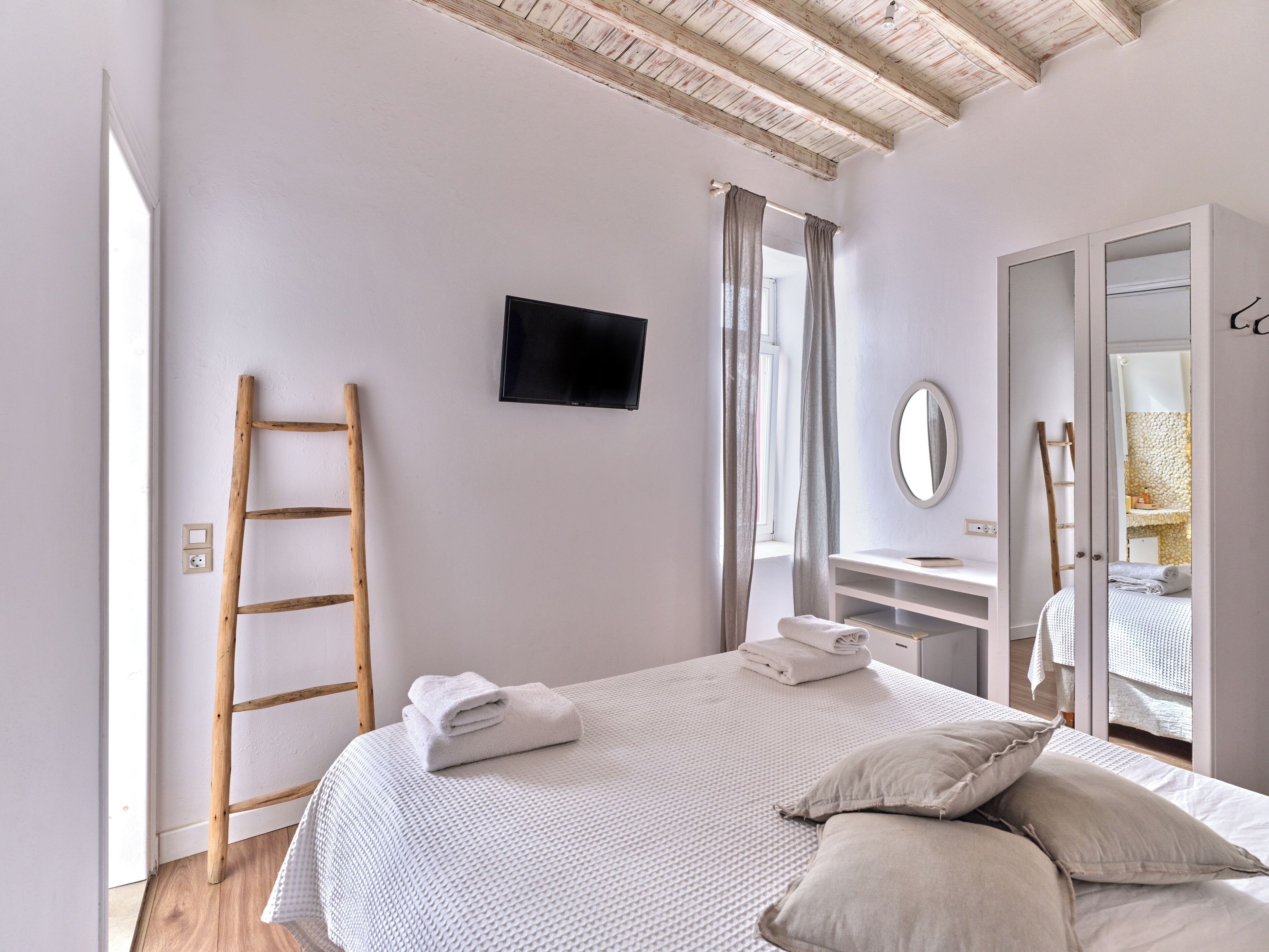 Un dormitorio con cama, televisor, espejo y armario.