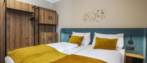 A hotel room with a large bed, wooden wardrobe, and a wall-mounted light fixture.