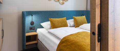 A neatly made bed with a blue headboard, two mustard-colored pillows, and a wooden nightstand with a lamp.