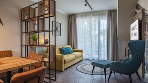 A modern living room with a wooden dining table, a sofa, a blue armchair, and a bookshelf.