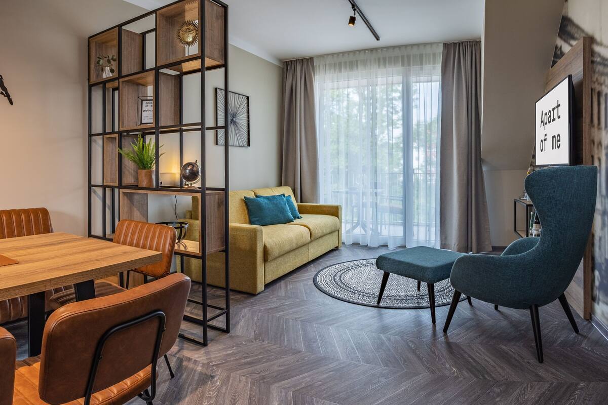 Una sala de estar moderna con una mesa de comedor de madera, un sofá, un sillón azul y una estantería.