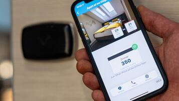 Smartphone che mostra un'interfaccia di prenotazione alberghiera con il numero di stanza 350, vista di una stanza con un letto e una finestra, e una maniglia della porta.