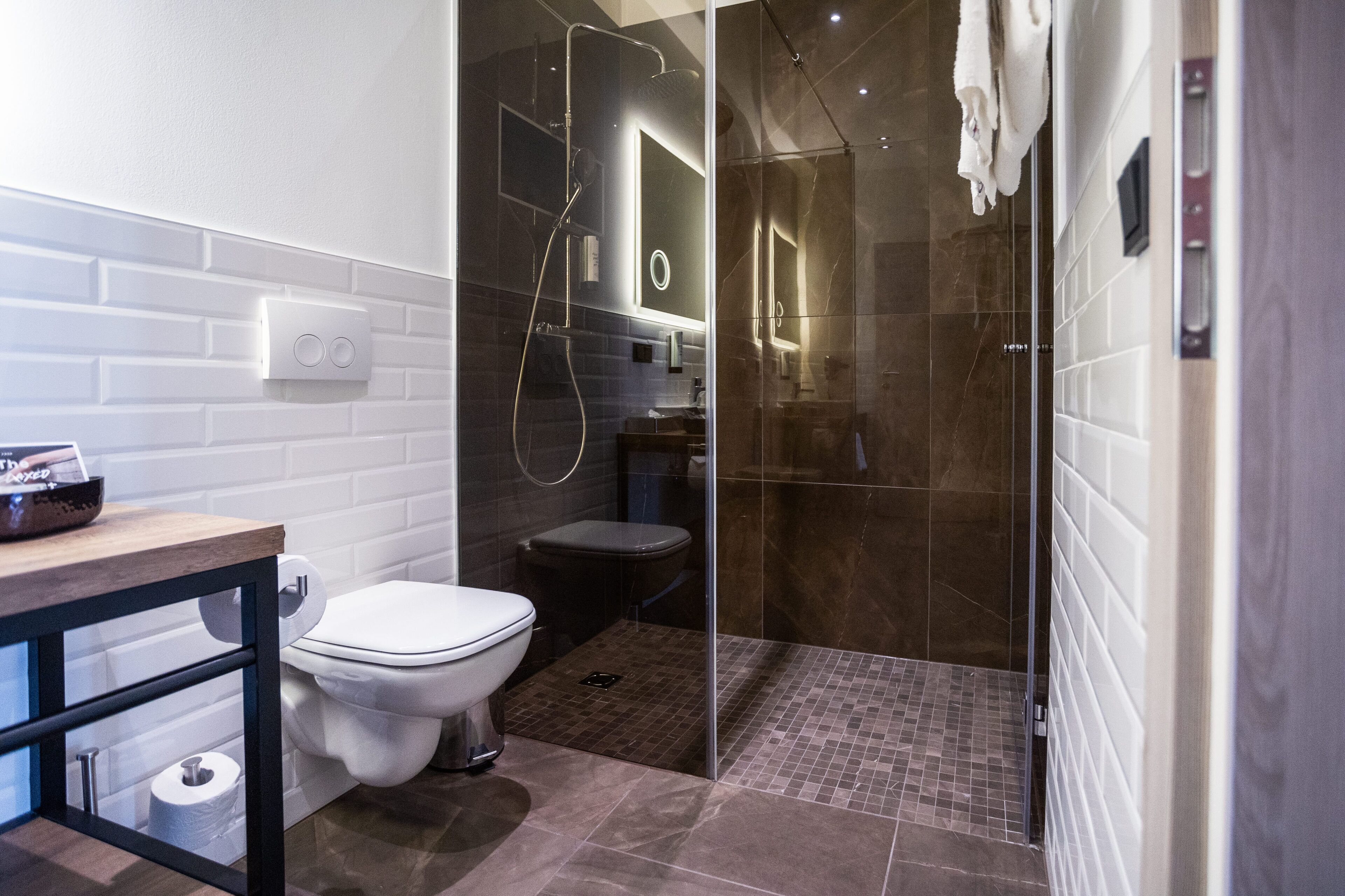 Un baño moderno con ducha envuelta en cristal, inodoro blanco y tocador de madera.