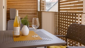 A table with a bottle of wine, a glass, and a small white vase with a plant on a balcony with wooden slats.