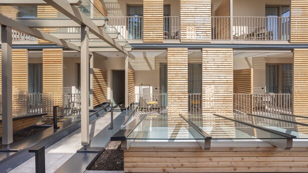 A modern multi-story building with balconies, a glass walkway, and wooden paneling.