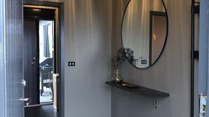 A modern bathroom with a wooden floor, a round mirror, and a shelf with a vase. - Hellnar Ocean View Villa (Hellnar)