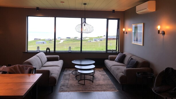 A modern living room with a large window, two sofas, a round coffee table, and a wooden table. - Hellnar Ocean View Villa (Hellnar)