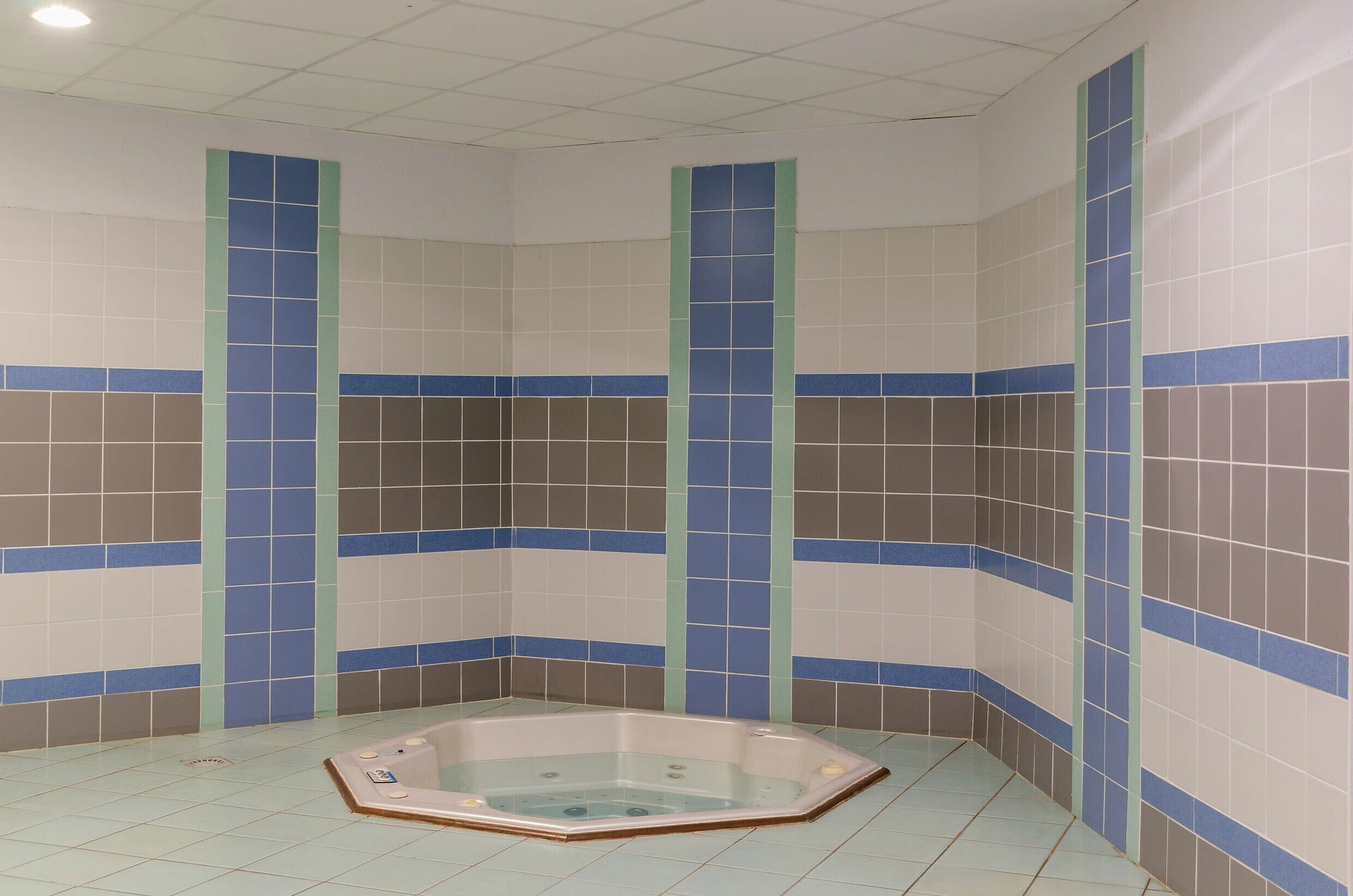 A corner bathroom with a bathtub, tiled walls, and a ceiling with a grid pattern.