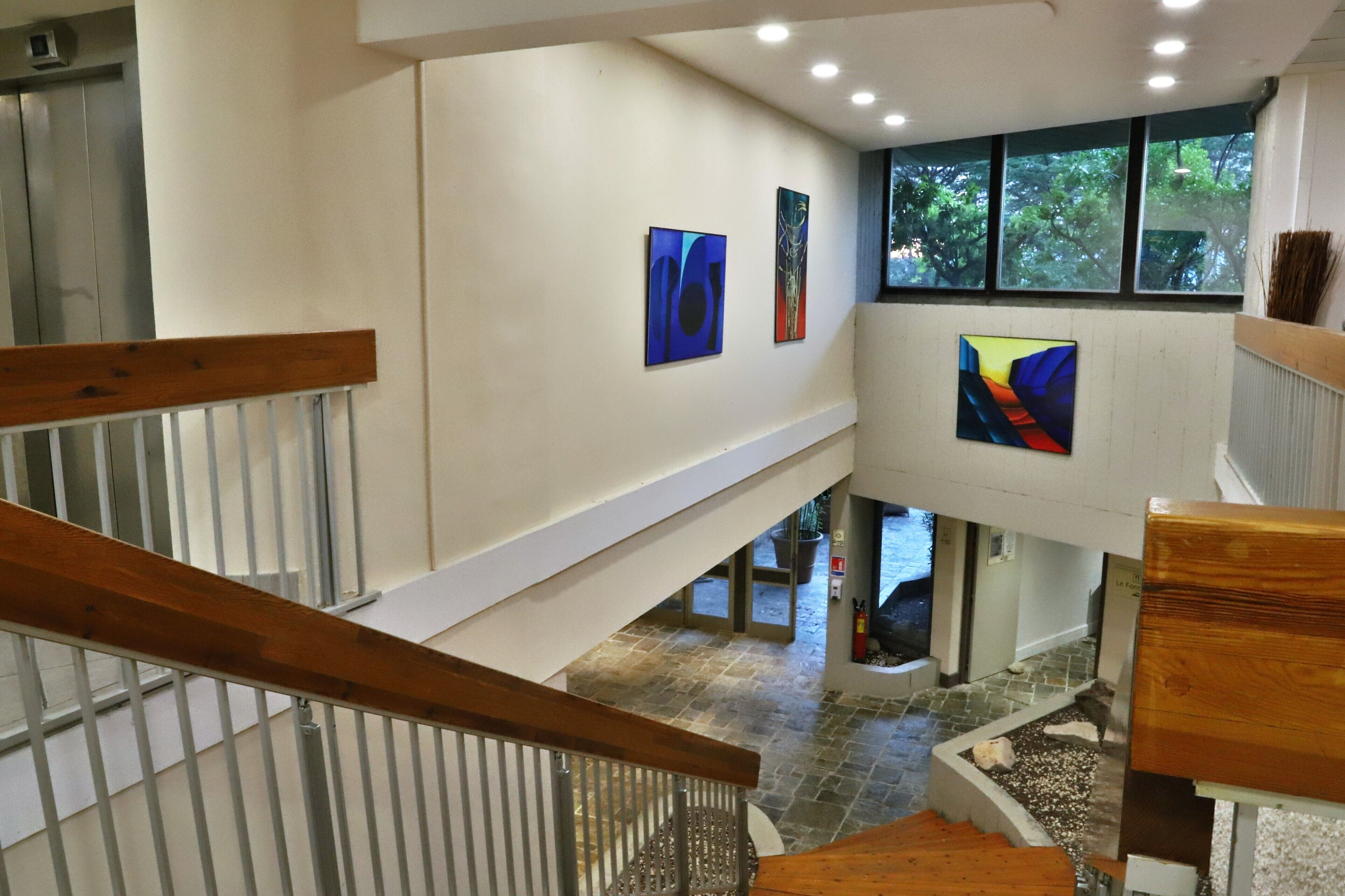 A modern interior with a wooden staircase, a stone floor, and abstract art on the walls.
