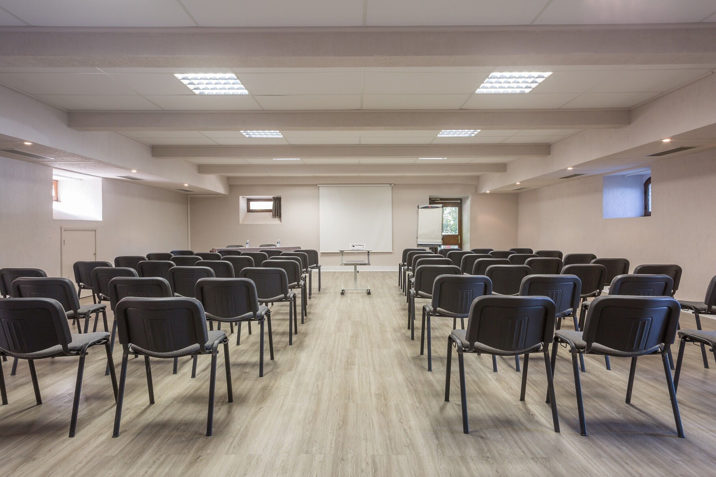 Une salle de conférence avec des rangées de chaises, un écran de projection et un tableau blanc.