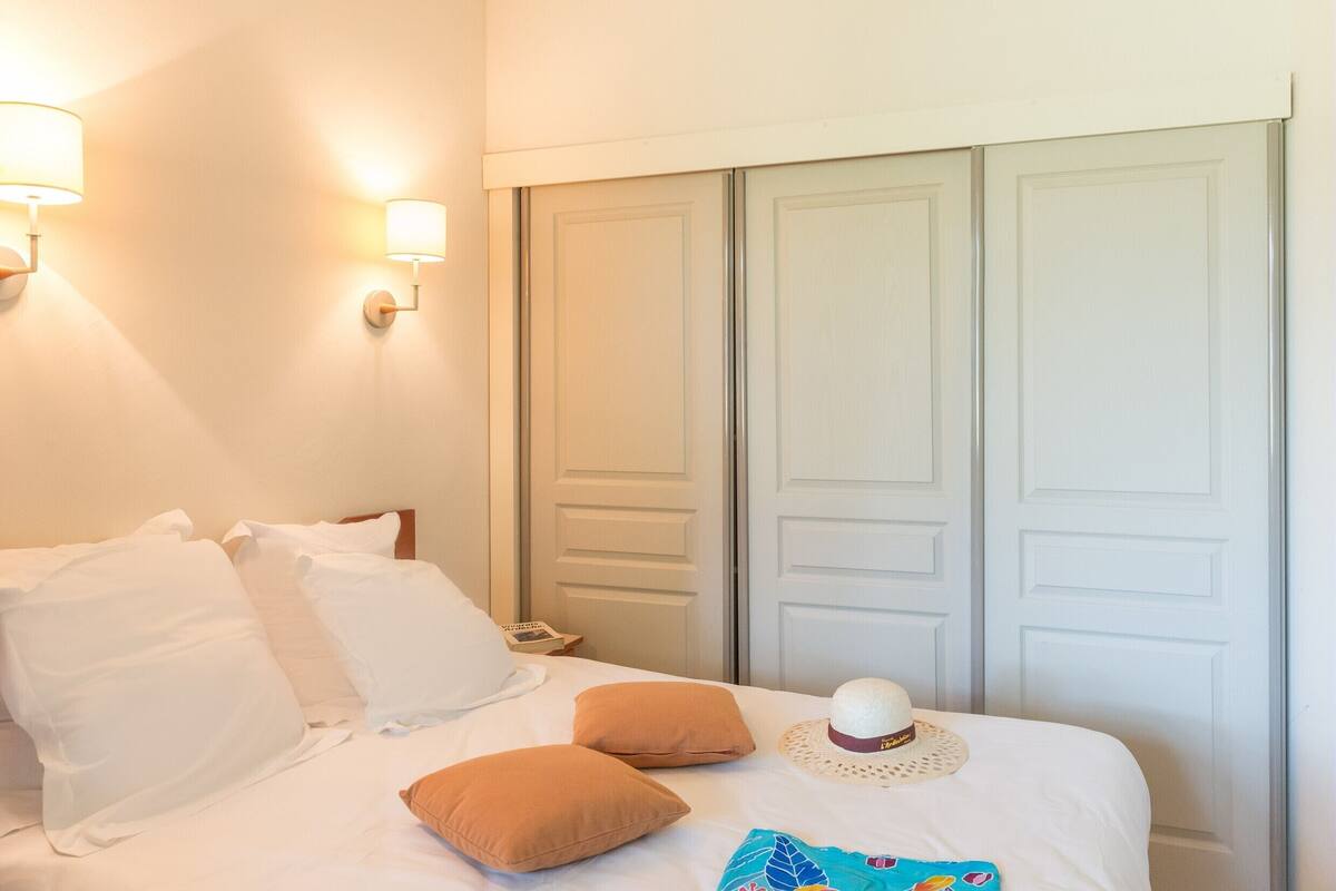 A neatly made bed with white and brown pillows, a decorative hat, and a colorful pillow.