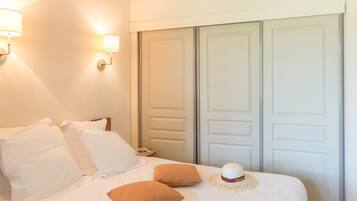 A neatly made bed with white and brown pillows, a decorative hat, and a colorful pillow.