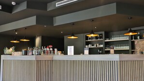A modern bar area with a wooden counter, pendant lighting, and shelves stocked with glasses and bottles. - SOWELL HOTELS Ardèche (Grospierres)