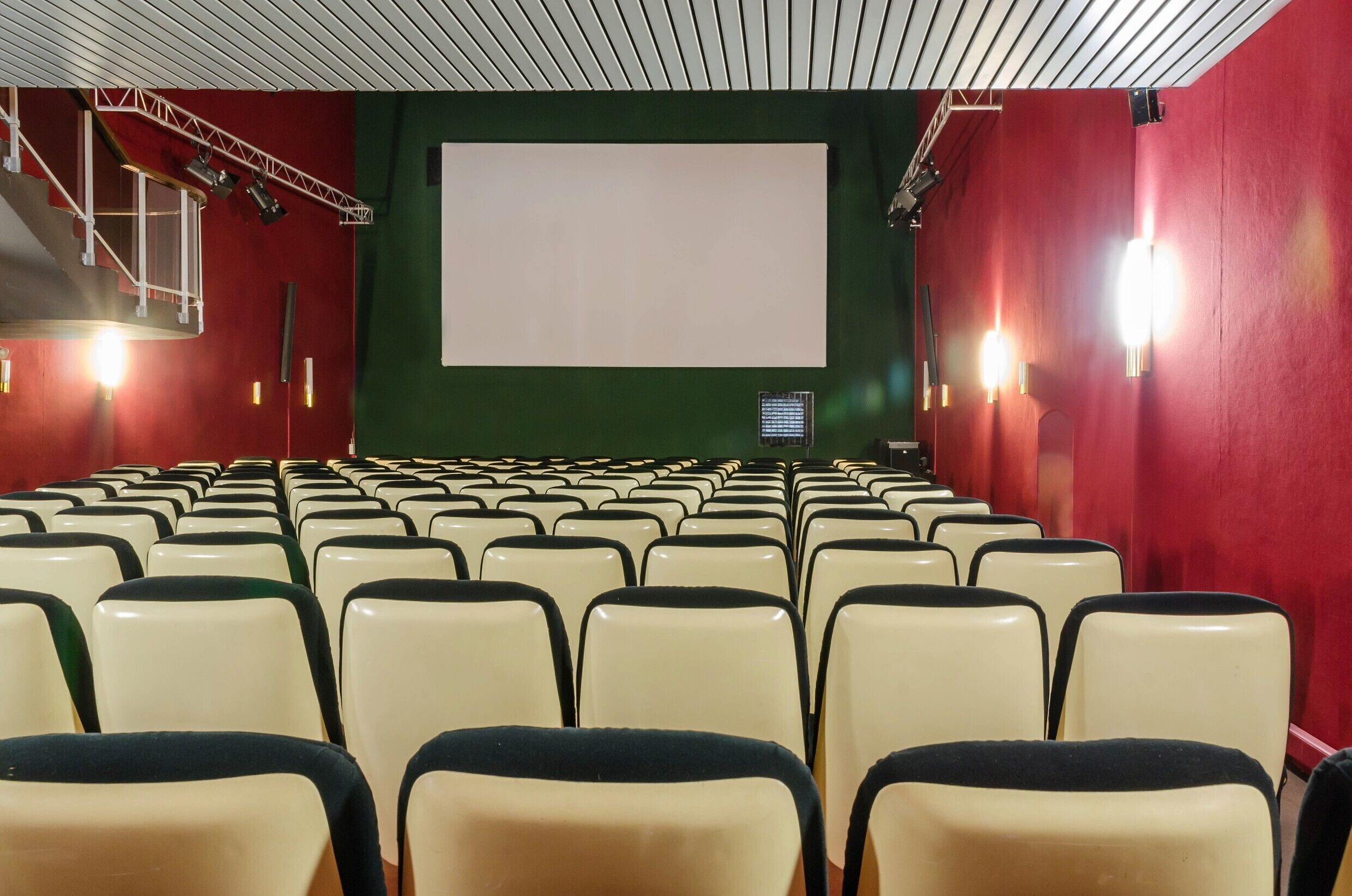 Une salle de cinéma avec des rangées de sièges disposées face à un grand écran, équipée d’un système d’éclairage et d’une console de contrôle.
