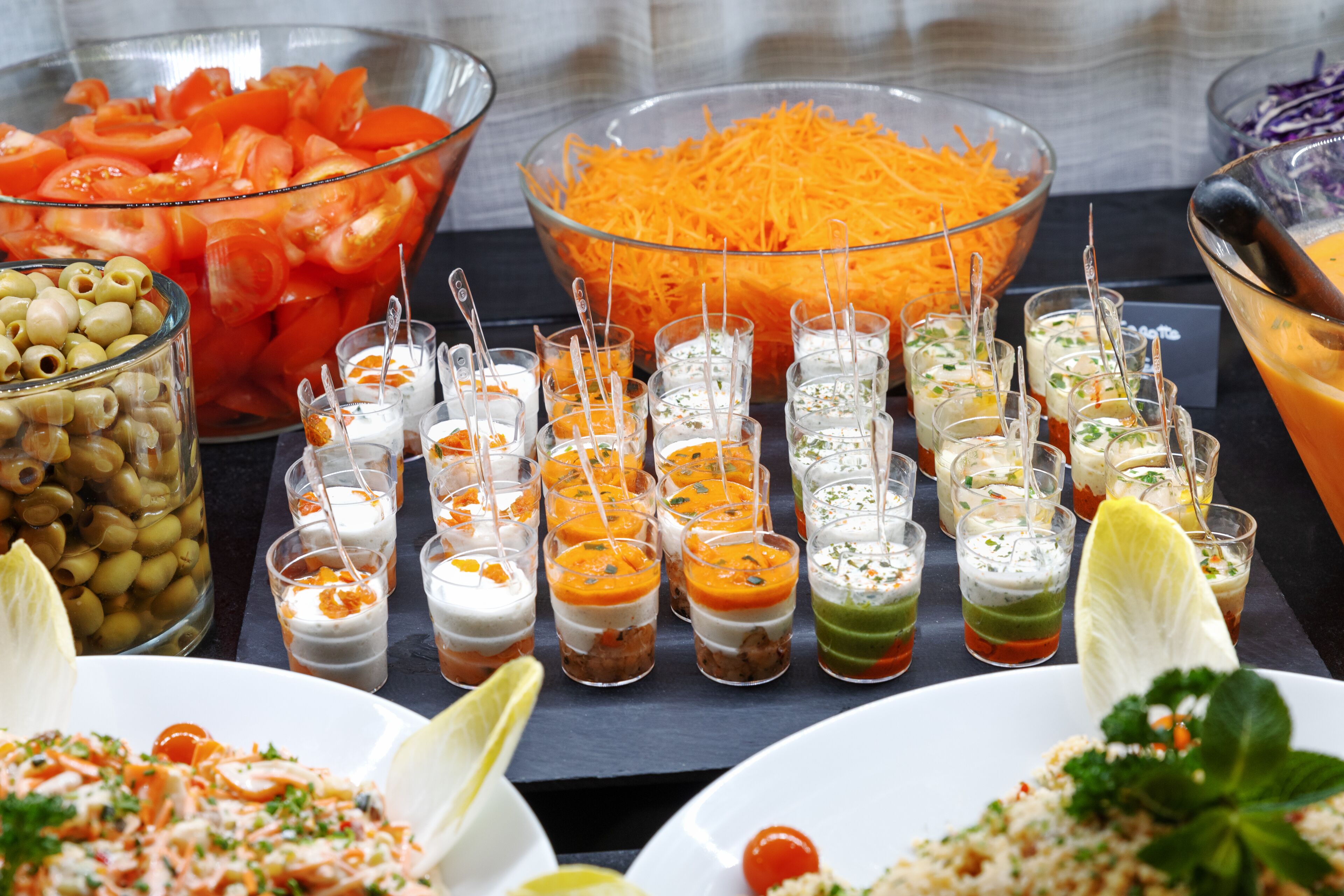 Una mesa de buffet con diversos alimentos, incluyendo tomates en rodajas, zanahorias ralladas y pequeños recipientes de salsas.
