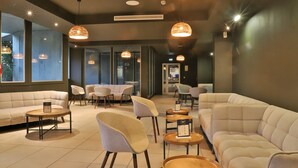 A modern lounge area with sofas, chairs, and round tables, featuring large windows and pendant lighting. - SOWELL HOTELS Ardèche (Grospierres)