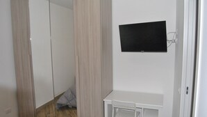Quarto com guarda-roupa, televisão na parede e pequena escrivaninha com cadeira.