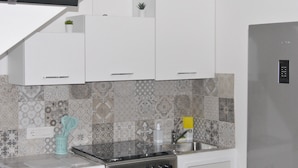 Uma cozinha moderna com armários brancos, pia de aço inoxidável e azulejos decorativos na parede.