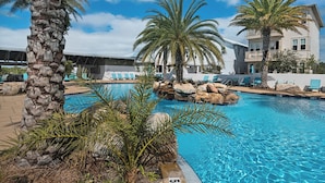 A swimming pool with palm trees and lounge chairs, surrounded by a building with balconies.