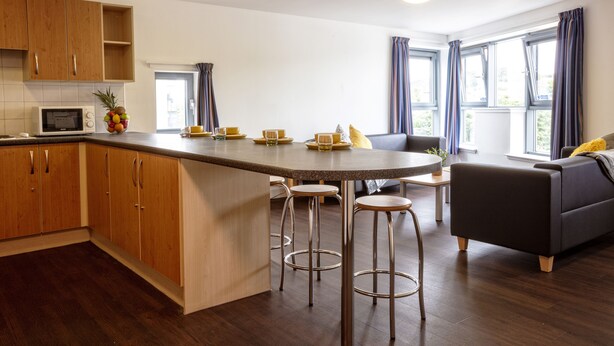 A modern kitchen with wooden cabinets, a central island with stools, a microwave, and a fruit bowl.