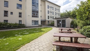 A courtyard with picnic tables, a building with multiple windows, and a small structure with a metal door.