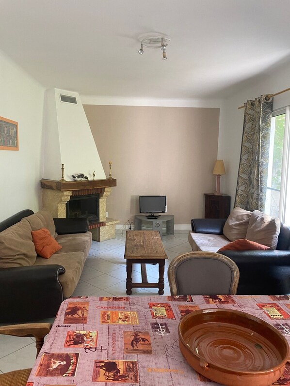Un salon avec une cheminée, un canapé, une télévision et une table recouverte d’une nappe à motifs.