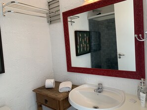 A bathroom with a white textured wall, a wooden vanity with a sink, a mirror with a red frame, and a towel rack.