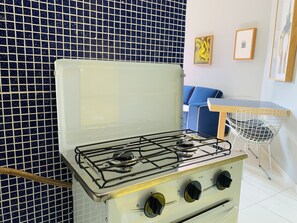 A kitchen with a gas stove, a blue tiled wall, a blue sofa, and a white chair.