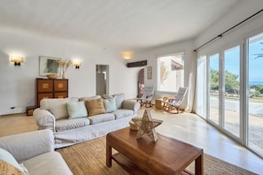 A spacious living room with a large sofa, a coffee table, and a view of the outdoors through large sliding glass doors.