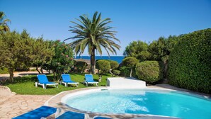 A pool area with blue lounge chairs, a palm tree, and a view of the sea.