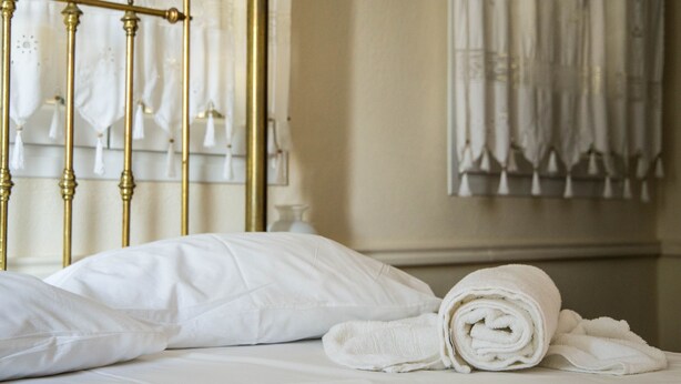 A neatly made bed with white linens and a rolled towel, a brass bed frame, and a window with curtains. - Villa Thalia Thassos Island Limenaria Greece (Thasos)