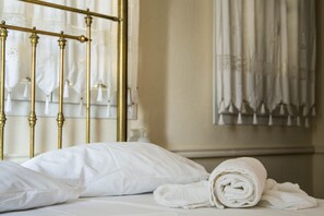 Un lit bien fait, avec des draps blancs et une serviette pliée, un cadre de lit en laiton et une fenêtre avec des rideaux.