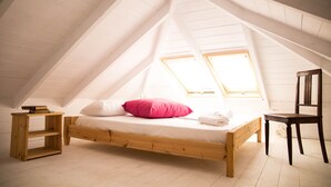 Una habitación con techos altos y un techo inclinado, una cama de madera con almohadas, una silla y una pequeña mesa de madera.