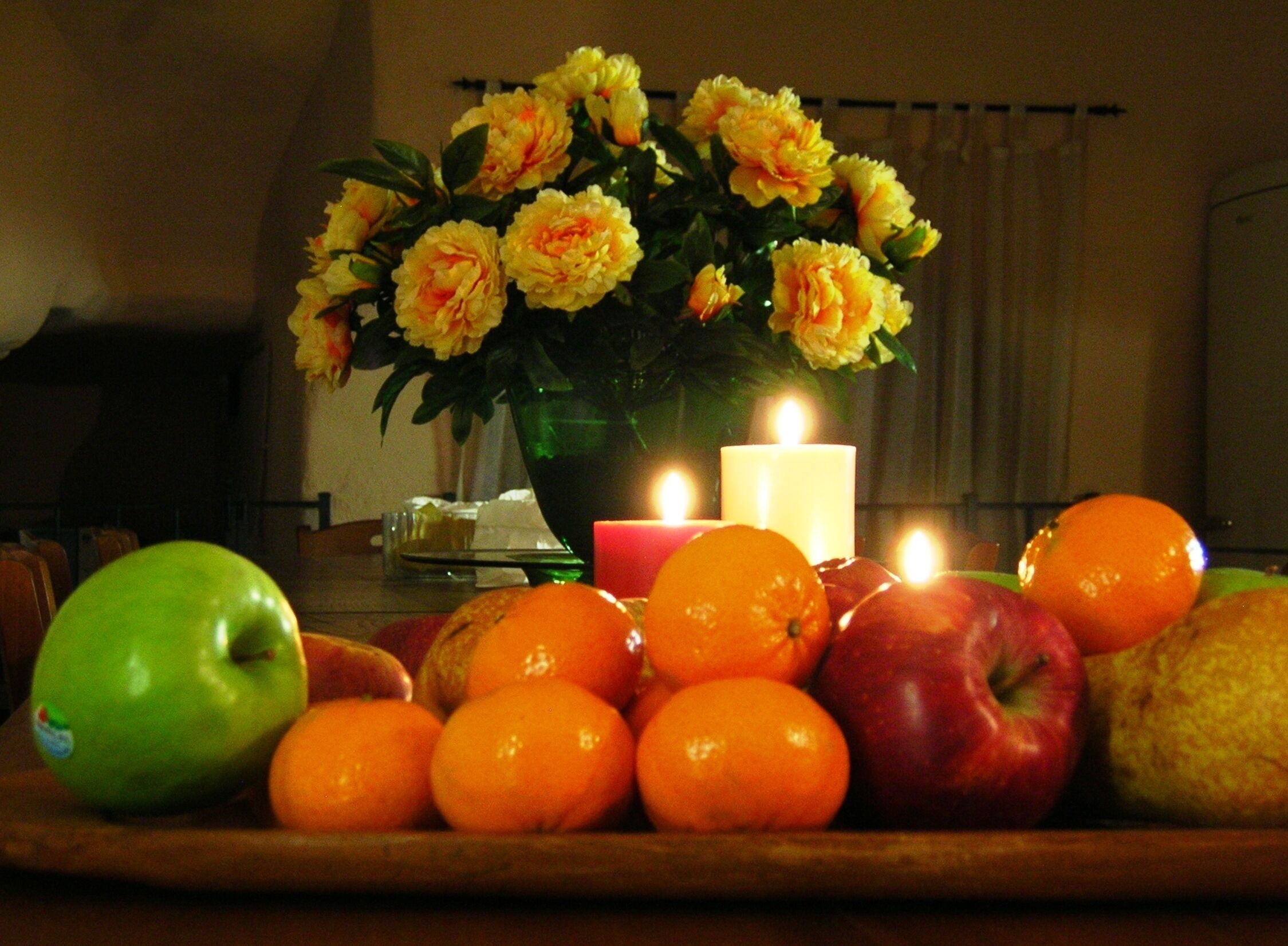 Una mesa con una composición de frutas, una vela y un florero.