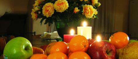 Una mesa con una composición de frutas, una vela y un florero.
