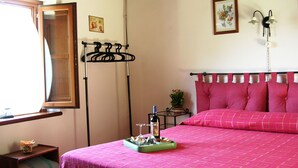 A bedroom with a bed, a bedside table, a window, a wall-mounted light fixture, and a small potted plant. - Ancient Rural Tower in Tuscia Area, Near Viterbo Italy (Vignanello)
