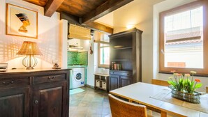 A kitchen with dark wooden cabinets, a washing machine, a dining table with chairs, and a window with blinds. - Best Located in Alghero old Town Steps to sea Attic Emerald (Alghero)