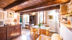 A cozy kitchen with wooden beams, a dining area with wicker chairs, and a sofa. - Best Located in Alghero old Town Steps to sea Attic Emerald (Alghero)