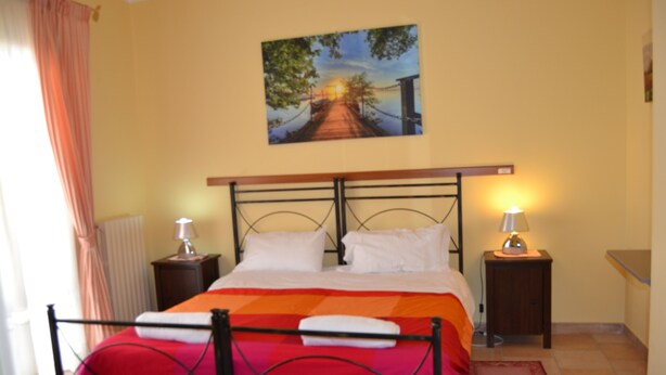 Une chambre à coucher avec un lit, deux tables de chevet, une commode, un tableau au mur et une fenêtre avec des rideaux.