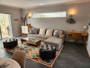 Un salon comprenant un canapé, des poufs, une table basse, un bureau et une chaise.